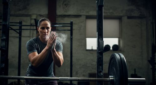 Ein Athlet kreidet seine Hände ein, im Hintergrund eine Hantel für den 5x5 Trainingsplan.