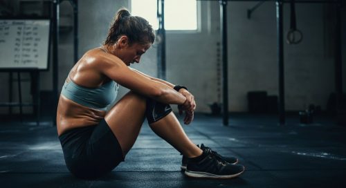 Eine erschöpfte Athletin sitzt nach einem der anspruchsvollen Benchmark WODs auf dem Boden einer Fitness-Box.