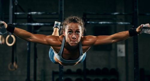 Eine Athletin in einer CrossFit-Box führt mit voller Konzentration einen Butterfly Pull-up aus.