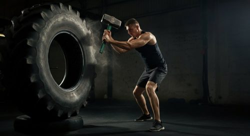Ein Kampfsportler macht explosives Crosstraining mit einem Vorschlaghammer auf einem Reifen.