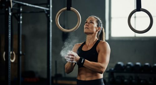 Eine Athletin kreidet ihre Hände ein und blickt konzentriert auf Turnringe für ihr Gymnastics Crosstraining.