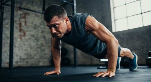 Ein Athlet in der anstrengendsten Phase einer Handstand Push Up Progression an einer Ziegelsteinwand, hochkonzentriert.