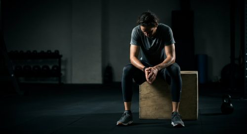 Nachdenklicher Athlet sitzt in einem Fitnessstudio und denkt über die Nachteile von HIIT wie Übertraining nach.