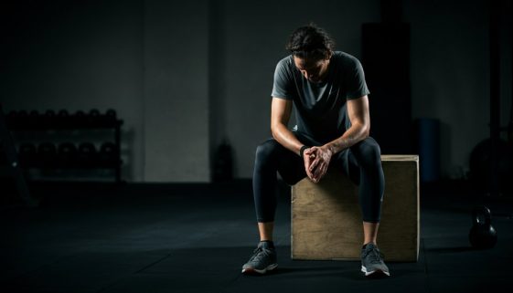 Nachdenklicher Athlet sitzt in einem Fitnessstudio und denkt über die Nachteile von HIIT wie Übertraining nach.