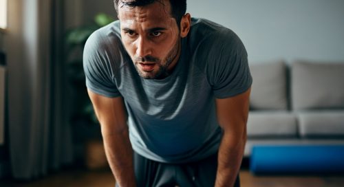 Mann macht eine Pause bei seinem intensiven HIIT Oberkörper Workout zuhause und stützt sich erschöpft ab.