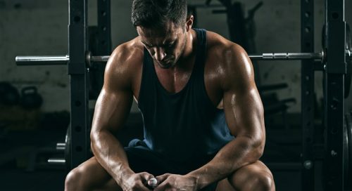 Ein athletischer Mann pausiert nach dem Training gemäß seinem Powerbuilding Trainingsplan in einem Gym.