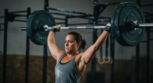 Eine Athletin hält nach dem Snatch lernen eine Hantel mit perfekter Technik über dem Kopf.