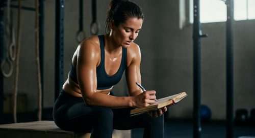 Fokussierter Athlet, der nach dem Workout sein Trainingslogbuch führt, um Fortschritte zu planen.