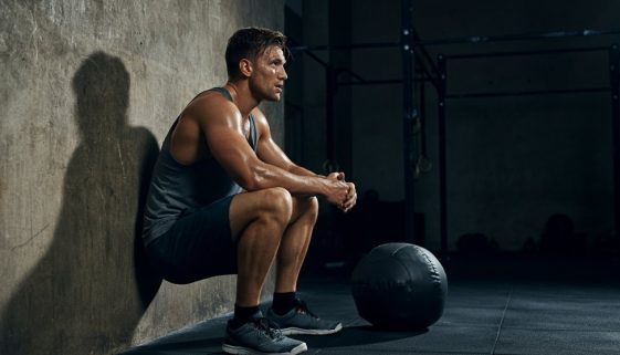 Erschöpfter Athlet lehnt nach dem Training an der Wand, was die Wichtigkeit der Wall Balls Technik zeigt.